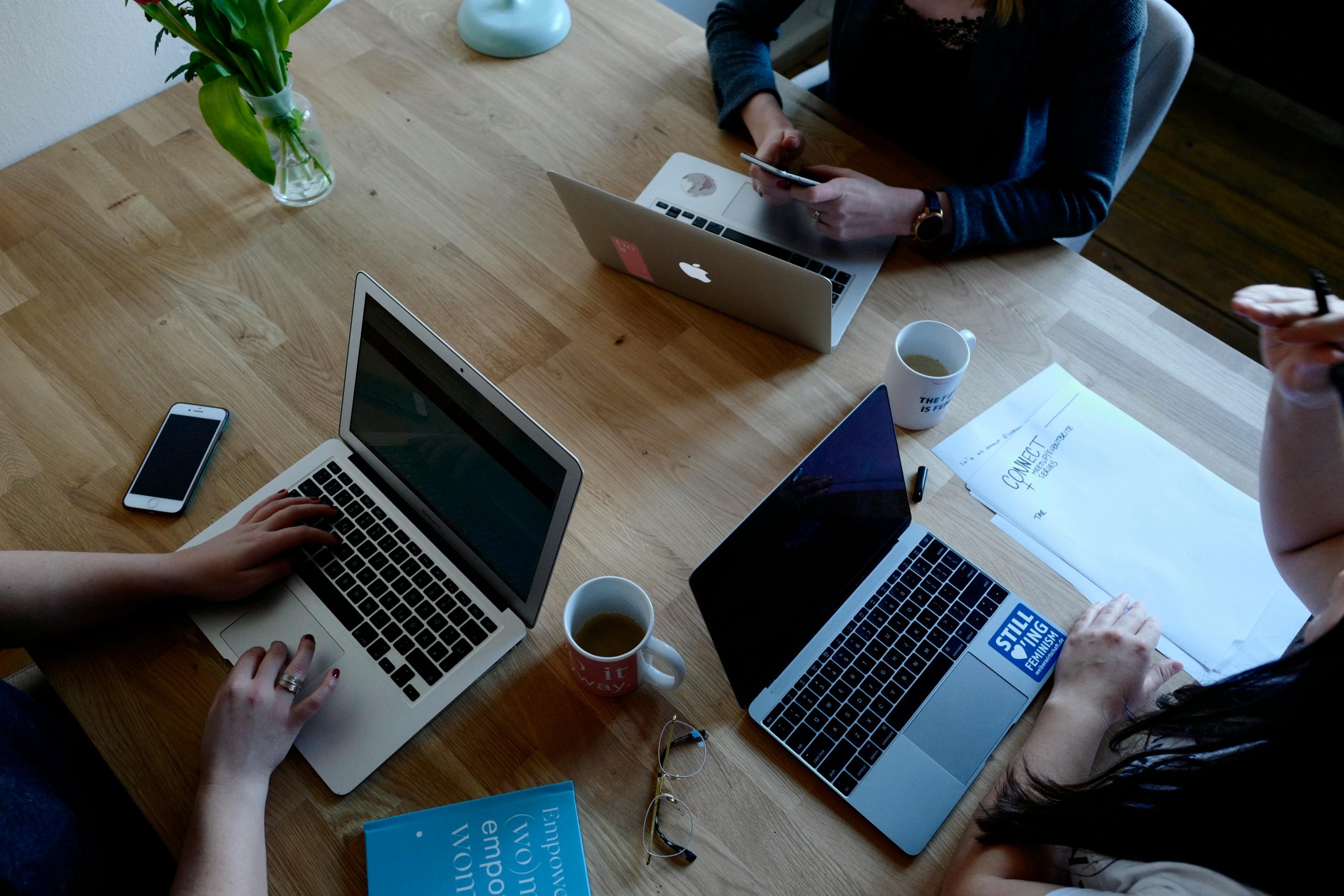 Overhead view of a modern workspace with laptops, coffee, and documents on a wooden table.